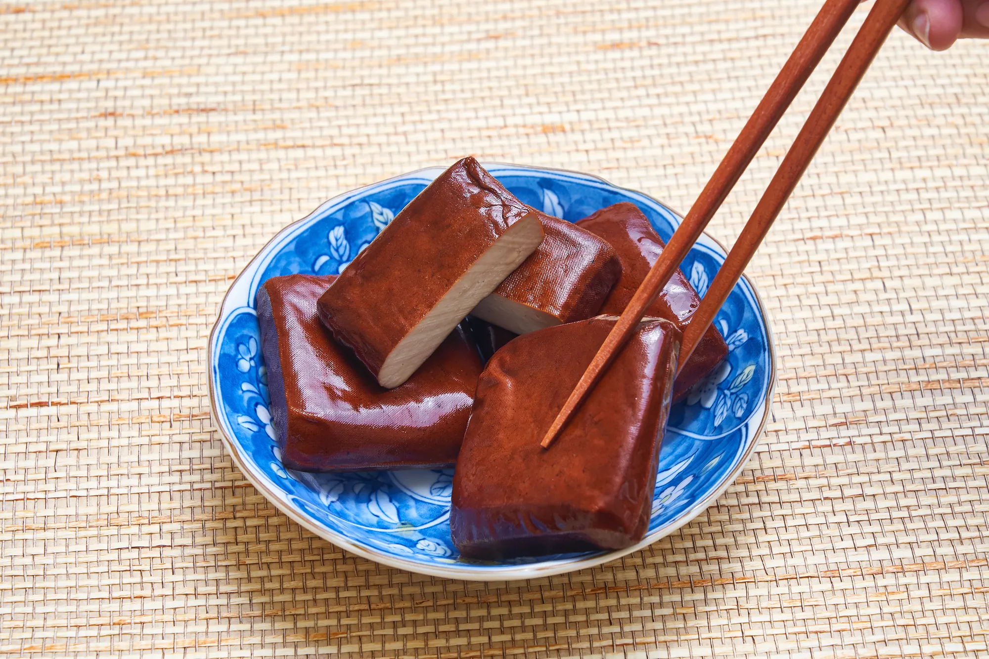中式青花瓷盤盛裝的桃園大溪滷黑豆干,質地扎實色澤深潤,筷子夾起切開斷面。