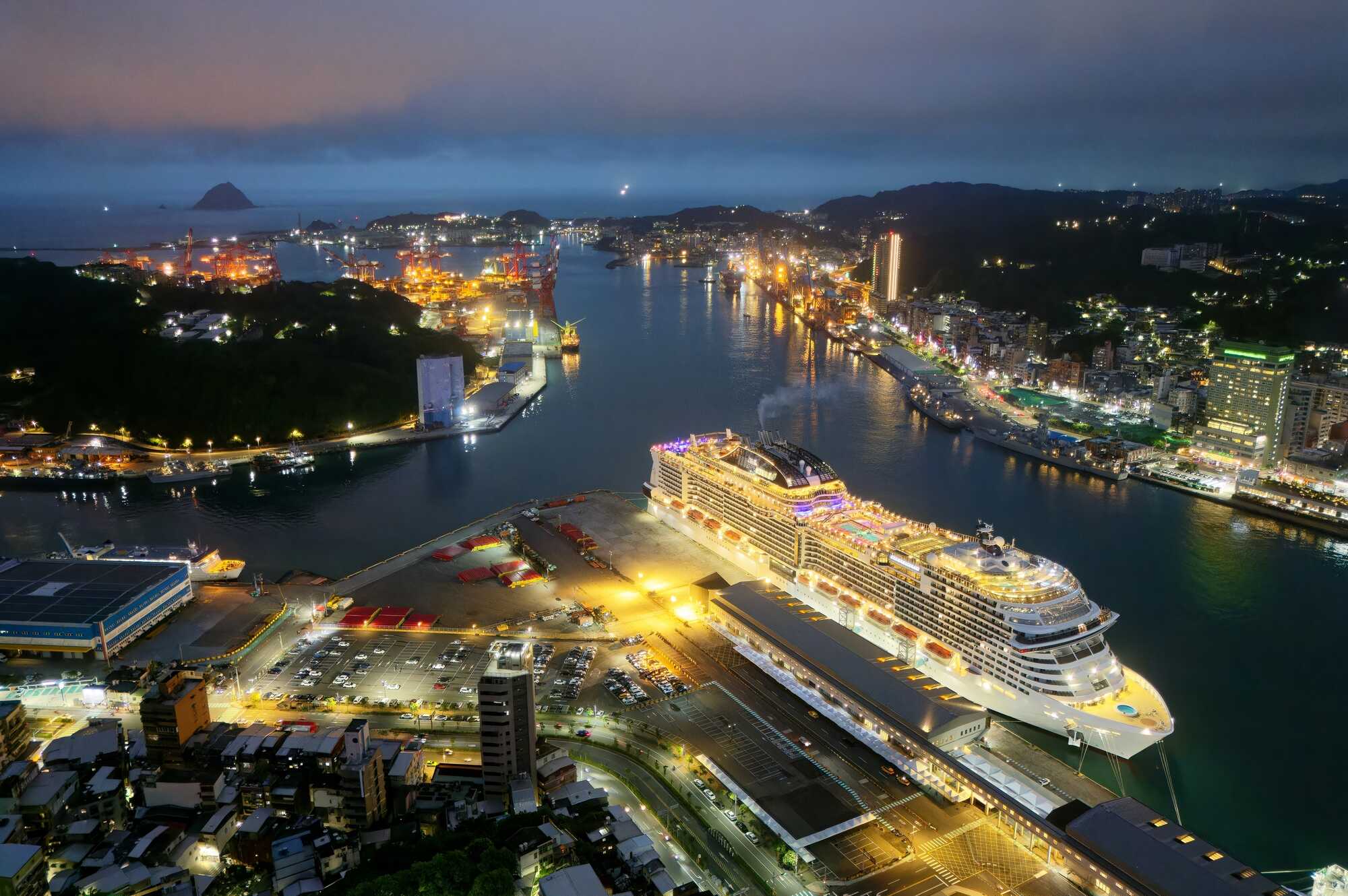 基隆港璀璨夜景空拍,大型豪華郵輪停泊於客運碼頭,背景為城市燈火與遠方的基隆嶼。