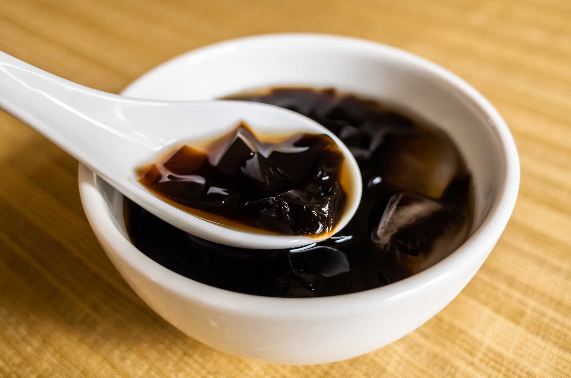 裝在白色陶瓷碗中的台灣傳統甜點仙草凍，白湯匙正舀起一塊晶瑩剔透的仙草。